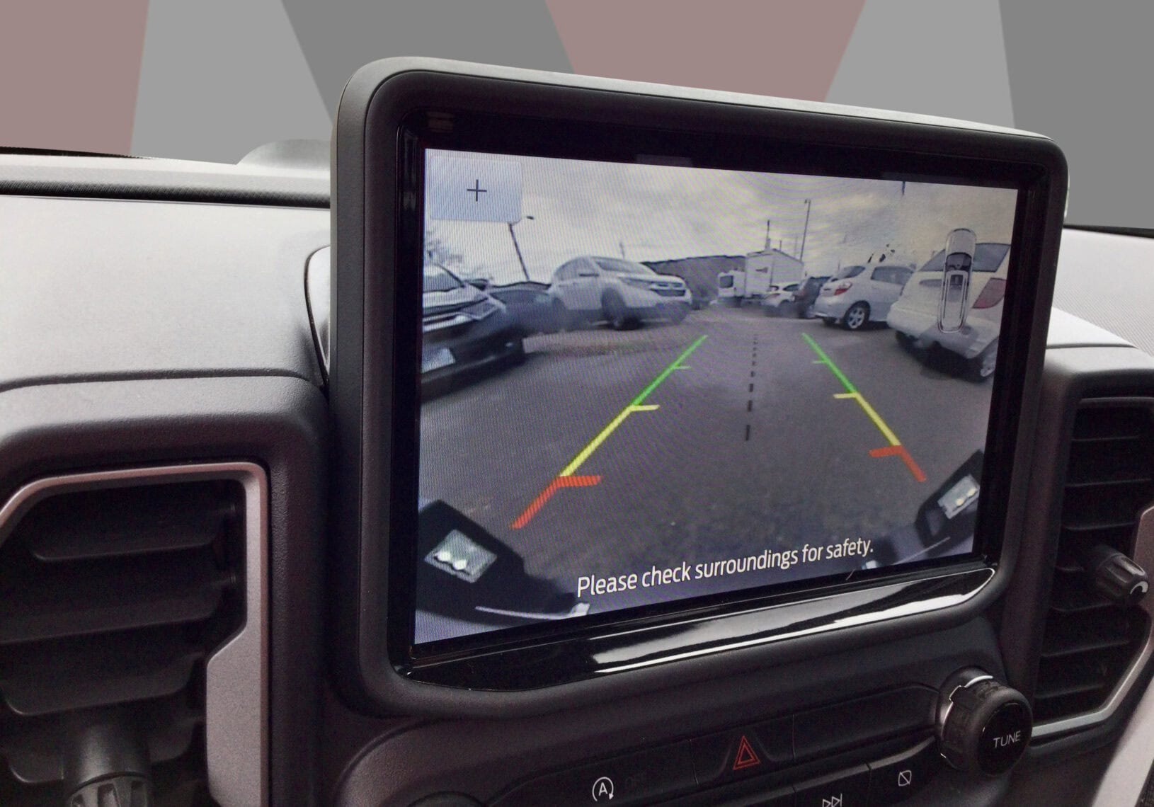 Backup camera view showing parking lot with vehicles and safety guidelines.