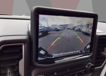 Backup camera view showing parking lot with vehicles and safety guidelines.